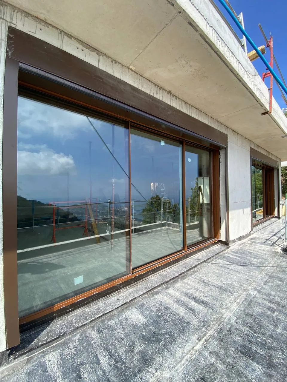 Großformatige Schiebetür mit braunen Profilen, frisch eingebaut in einem Haus im Bau mit Meerblick